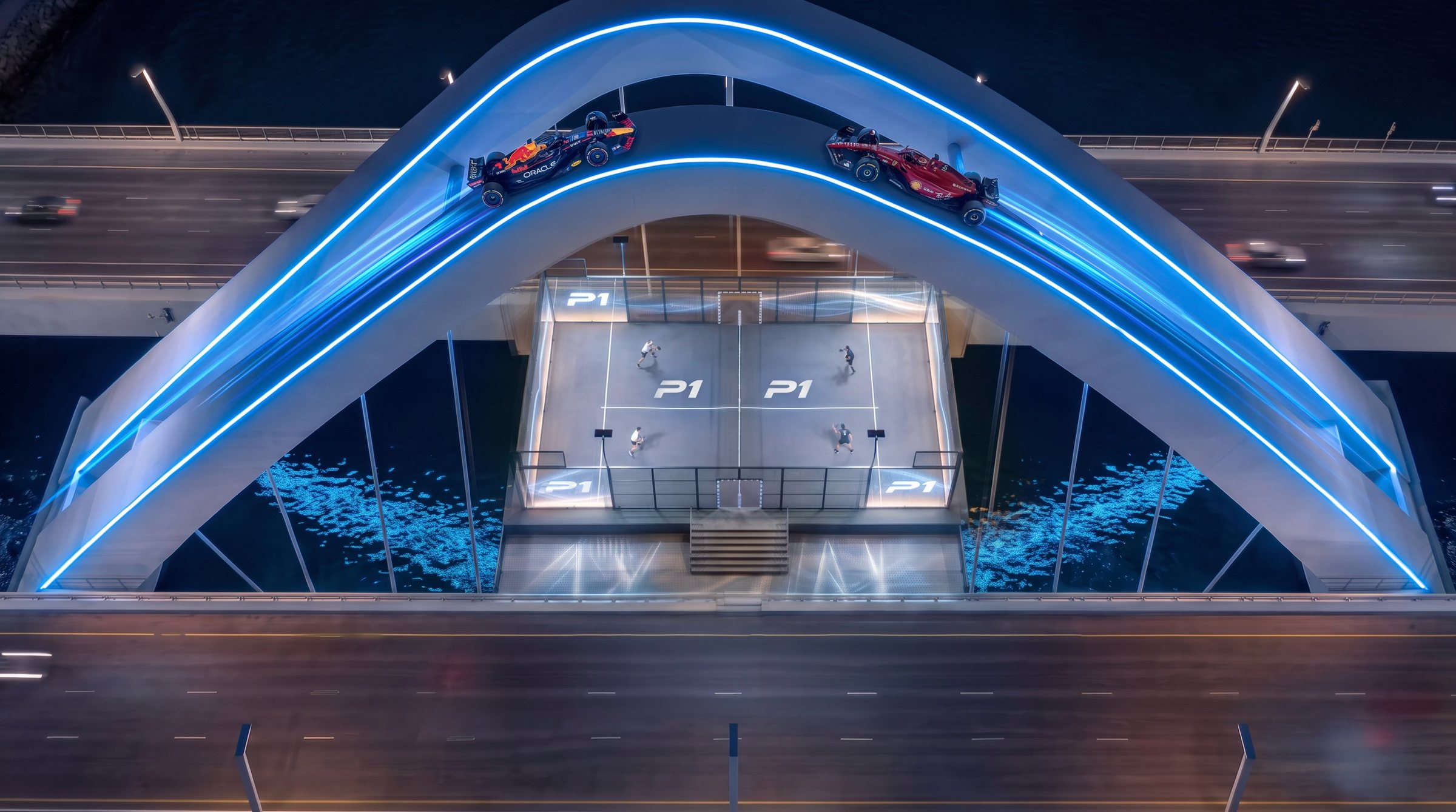 Top-down view of the suspended court as two F1 cars race over the blue-lit arch